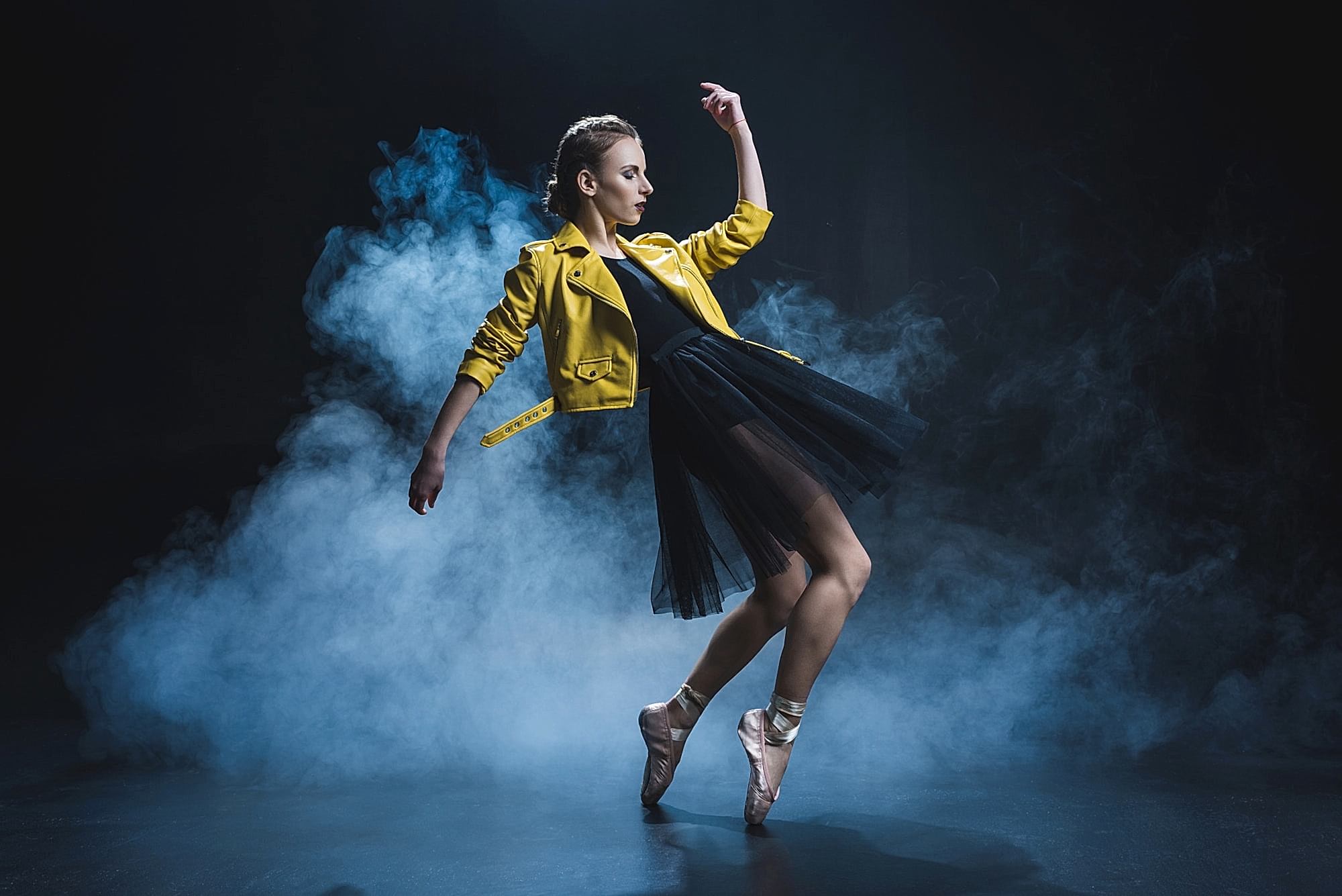 attractive girl dancing in pointe shoes and black tutu and yellow leather jacket in studio with